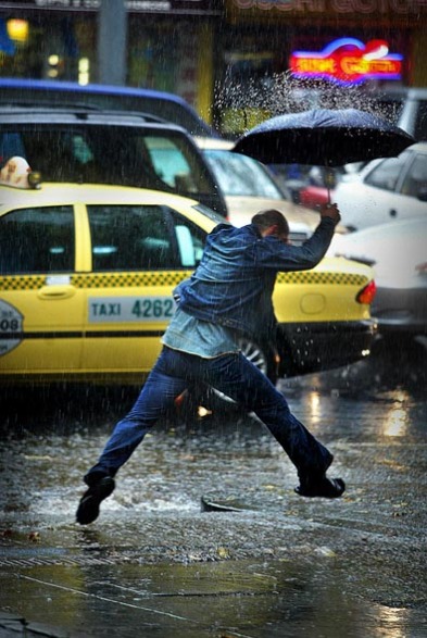csz030413.001.001.jpg The Age NEWS  Lonsdale street Melbourne, the heavens open up with rain as a man with a umbrella tries to leap water running down a driveway. 13th April 2003. S Picture By Craig Sillitoe